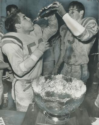 Gaels Sip Champagne, Donald McIntyre (73) helps teammate Stephen Davis hold bottle of the bubbly as Queen's University players celebrate in clubhouse (...)