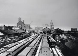 Image shows trains on tracks with some buildings in the background.