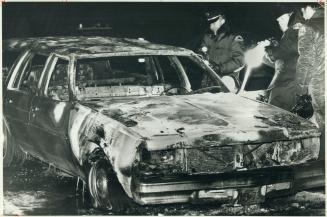 Metro police and firemen examine the charred and blast-buckled wreck in which a man died
