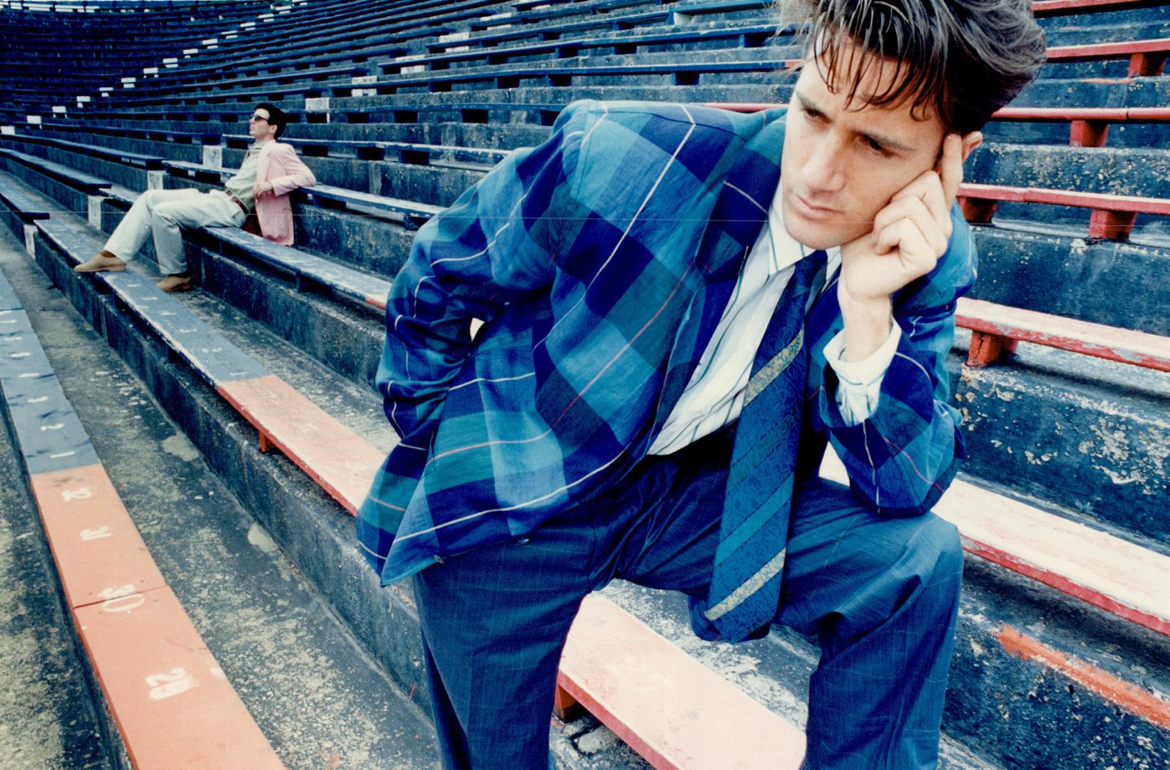 Above foreground, lightweight checked linen sports jacket in shades of blue, $350, is worn with a bright green and white striped shirt, $120, blue tro(...)
