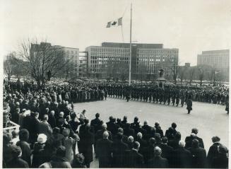 An honor guard stands to attention as hats are doffed and men in uniform salute the new maple leaf flag flying at Queen's Park. A 100-man guard of hon(...)