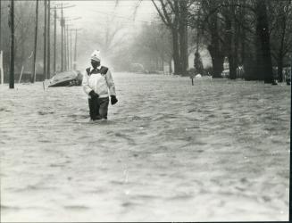 Main street -- St. Clair Beach, With his car in a ditch a flood victim makes his way along Riverside Drive, the main street in St. Clair Beach about 15 miles east of Windsor