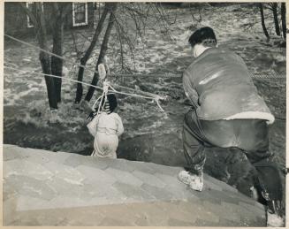 Riding to safety in an improvised breeches buoy, Robin Thompson, three, was the first to be rescued by this method in the Long Branch flood. [Incomplete]