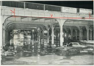 Image shows a part of the street under the bridge flooded with a car floating around.
