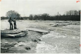 The Rain-swollen credit river engulfs Memorial park in Streetsville, where it swept away four footbridges, on of them where the youths are standing. [Incomplete]