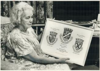 She designs Heraldry: Dorothy Stone holds painting she did of three coats of arms she designed