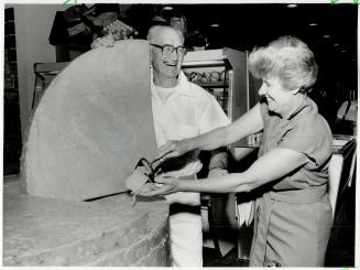 Big cheese, Joan Leslie takes the first slice from a 3,000-pound cheddar made by her father Frank at his cheese factory in Stratford