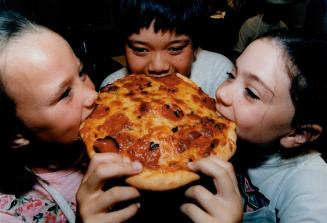 Tastes good: Sabrina Clark, 9, Butch Borromeo, both of Oakville, and Nancy Silverman, 9, of Thornhill, bite into a pizza they made when Kid-summer visited the Bonnie Stern cooking school