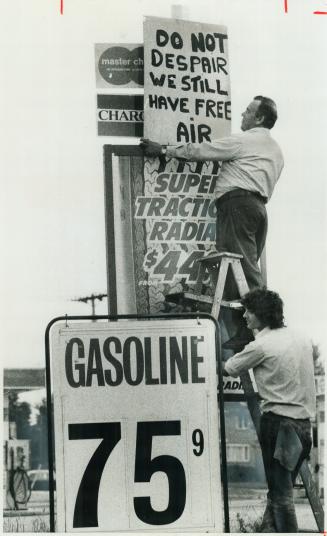 Taking a jab at gasoline price increases, Bill Coveyduck puts up a sign outside his service station in Scarborough while Larry Krosowski holds the ladder