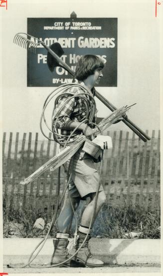 Carrying his tools, Hartley Woodside, 26, gets set to plant his garden in a plot he's renting on Leslie St