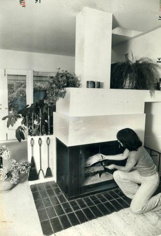 Betty Volgesi puts wood in her free-standing fireplace which acts as a room divider in her Douglas Dr. home