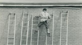 Don't try this at Home. This man uses an unusual technique to move horizontally along a wall while putting up trim on the eaves of a house on Strathmo(...)