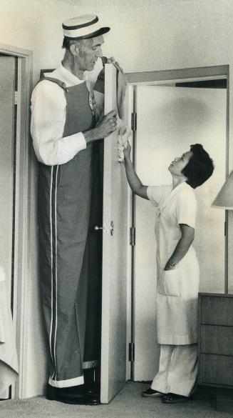 A man to look up to, Henry Hite, at 8-feet-2 claimed to be world's tallest man, has better vantage point than housemaid Teresa Gamboa for seeking dust on top of door at Four Seasons Sheraton Hotel
