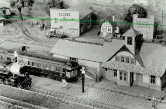 A model train pulls into a model station, so complete in detail that there are even miniature passengers waiting for the express