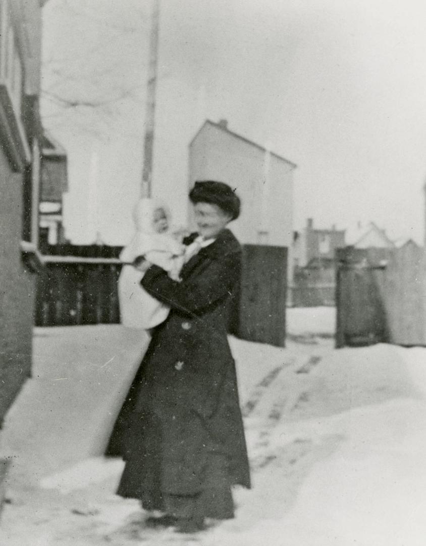 Image shows Mrs Eric Owen (Elsie MacLean) and baby daughter, Sheila Owen outside in winter.