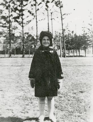 Image shows a girl on the lawn in winter. There are some trees in the background.