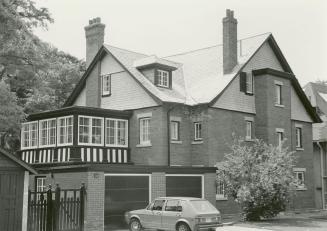 Image shows a three storey residential house with garages on the left. There is a car parked in ...