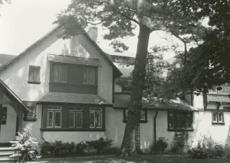 Image shows a two storey residential house. There are a few trees in front of it.