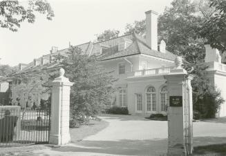 Image shows the gates and a partial view of a big residential house with some around it.
