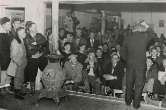 Stones were hurled at Premier Smallwood for his action at outlawing the IWA on the island. Union leader Harvey Ladd is shown addressing the jam-packed hall