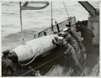 Hauling in the Paravane, a device used in sweeping the vital shipping channels clear of destructive enemy mines, slicker-clad sailors aboard a mineswe(...)