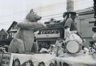 Children lining balcony of house, centre, watch happily as this huge bear pulls beard of an equally large elf on one of the many floats in the Santa C(...)