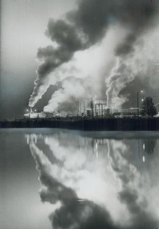 Mirroring a refinery, Spewing smoke into the air, the Texaco refinery at Port Credit is reflected in the glassy waters of an adjoining pond, created b(...)