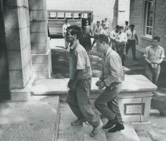 Kingston prisoners with their wrists handcuffed and wearing leg irons shuffle into Frontenao County courthouse yesterday, where the 18 men were remand(...)