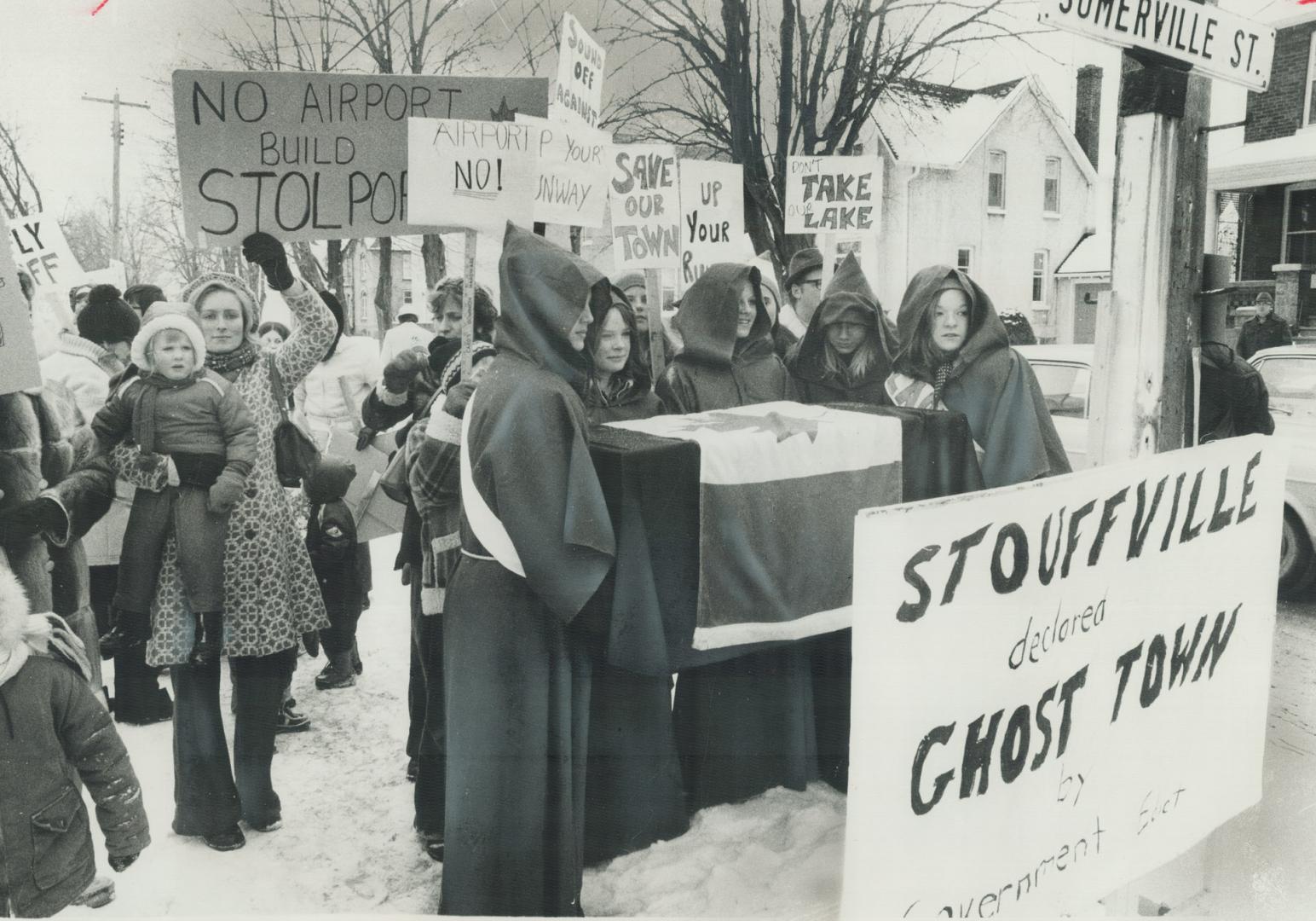 A coffin symbolizing the death of Stouffville was carried by boys and girls in monks' robes yesterday in a protest march on town hall to express fears(...)