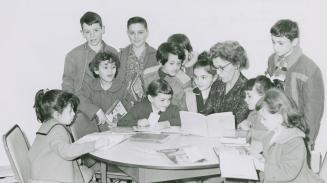 Group of children gathered around a table in the library with adult reading to them