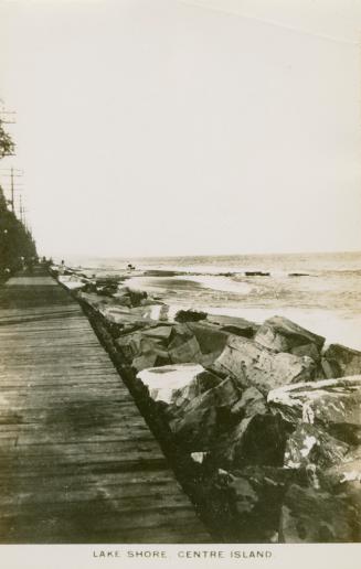 Black and white picture of wooden boardwalk and rocks and lake. 
