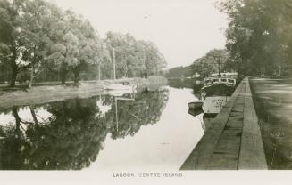Photo of tree lined lagoon with boats docked at the sides. 
