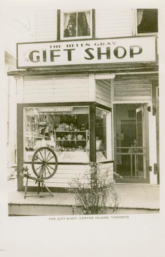 Picture of the storefront and window of a gift shop with a spinning wheel out front. 