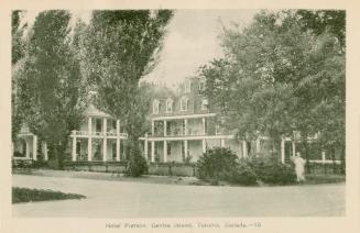 Photo of a three storey hotel with large balconies hidden behind several tall trees. 