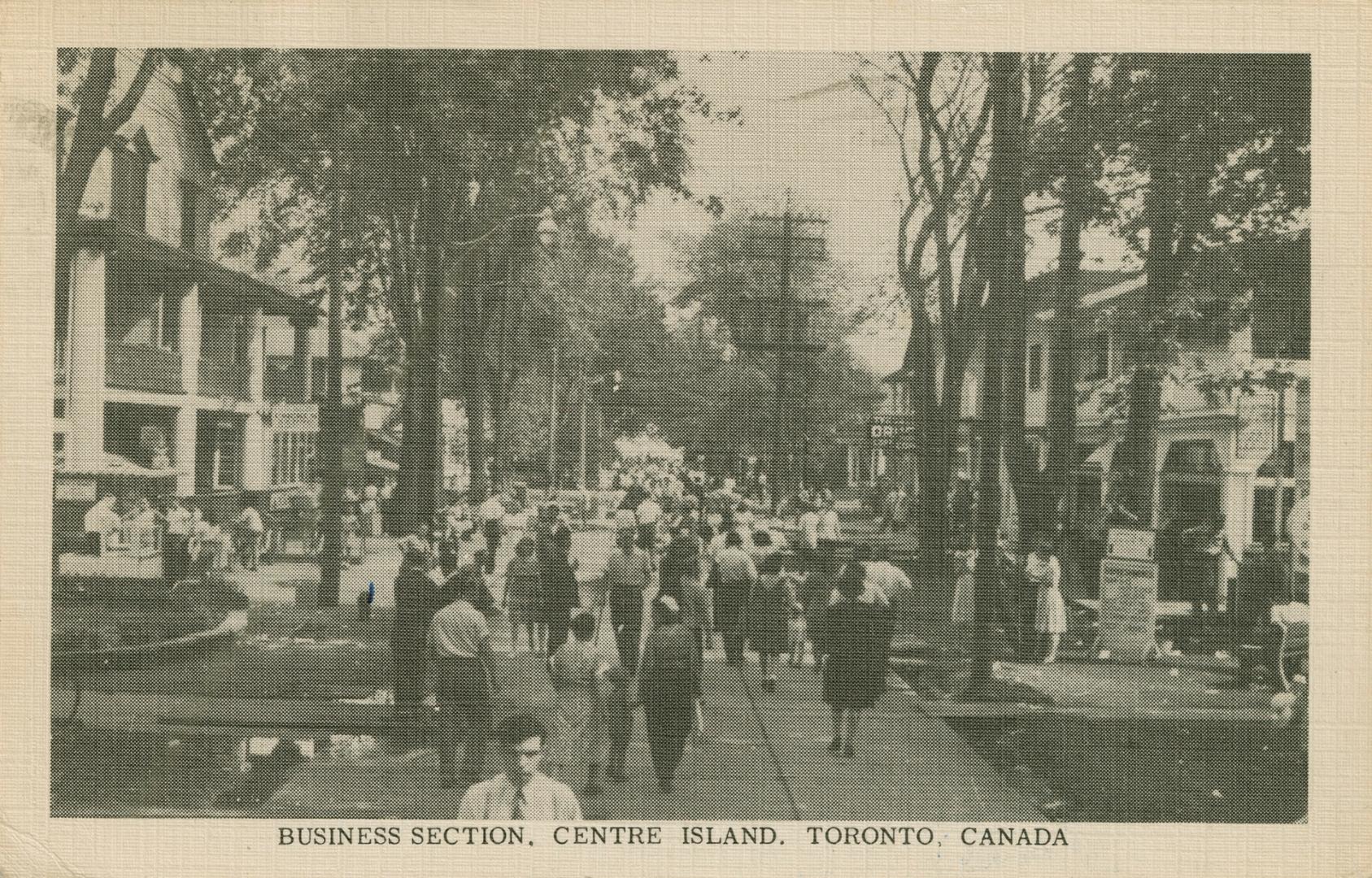 Photo of people walking down a street with hotels and shops on each side. 