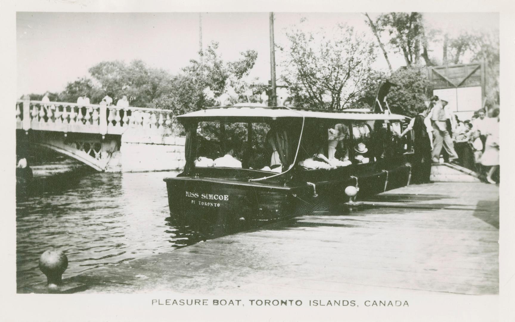 Photo of a sightseeing boat at a dock loading passengers and people watching from a low bridge …