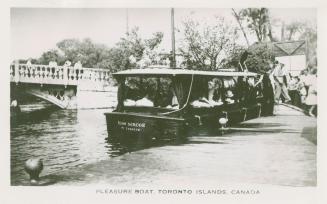 Photo of a sightseeing boat at a dock loading passengers and people watching from a low bridge …