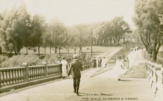 Picture of people walking over a bridge with park and trees in the background. 