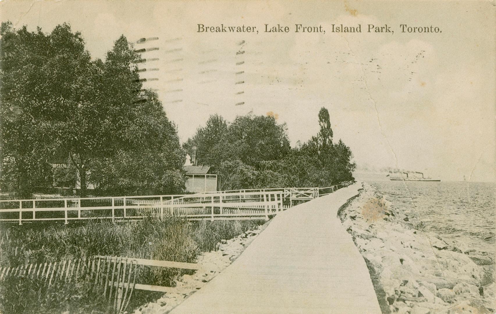 Black and white photograph of a lakefront with a plank boardwalk running along side it.