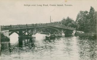 Black and white picture of two people in a canoe paddling under a bridge.