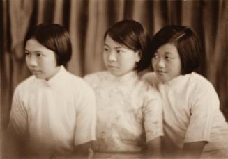 Three young women sitting next to each other in front of a curtain. 