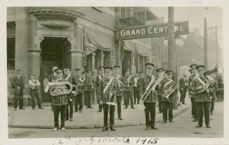 Black and white picture of member of a brass band in uniform, with instruments standing in fron ...
