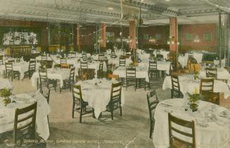 Color picture shows many table set for formal dining service in a very large room.