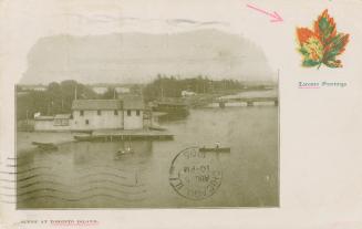 A wooden building and dock, with several canoes nearby. In the background, a wooden bridge span…