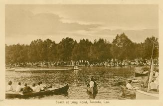 Sepia toned photograph of many people in large canoes. Many spectators line the shore.