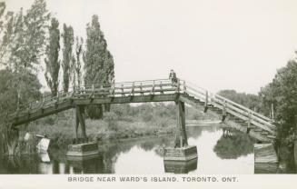 Black and white picture of a man standing on a wooden bridge crossing a lagoon.