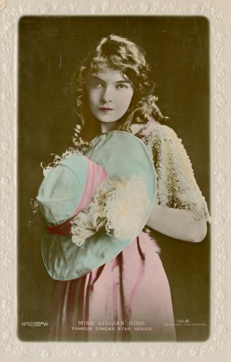 Hand tinted picture of Lillian Gish in a loose dress carrying a hat.