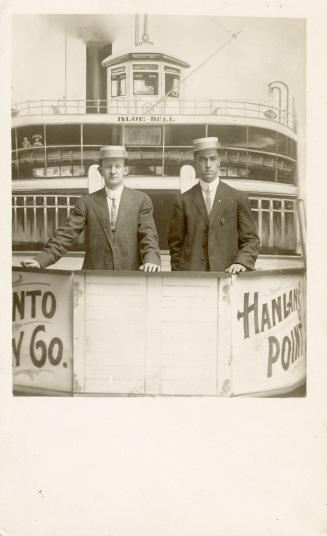 Black and white photograph of two men in straw boaters looking out form the back of a large boa…