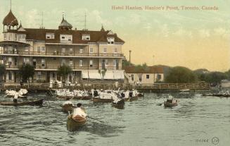 A very large Victorian hotel with people in row boats on the water in front of it.