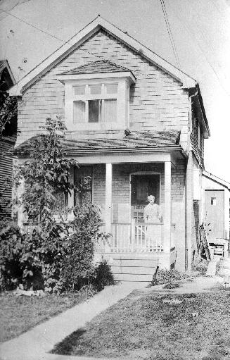 A photograph of a two-story house with a woman standing on the front porch.